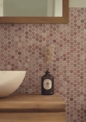 Un lavabo blanc posé sur un meuble en bois, devant un mur de petites mosaïques hexagonales brunes. Un flacon de savon est posé près du mur.