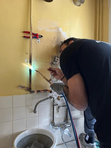 Tuyau d'évacuation blanc en PVC coudé fixé au sommet d'une chaudière murale blanche dans un espace intérieur.