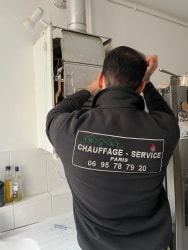 Une personne de dos, vêtue d'une veste noire avec une inscription, marche sur une allée pavée dans un jardin enneigé à Paris.