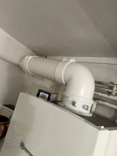 Tuyau d'évacuation blanc en PVC coudé fixé au sommet d'une chaudière murale blanche dans un espace intérieur.