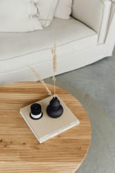 Table en bois clair avec un livre, une bougie noire et un vase noir avec des herbes sèches sur une surface grise. Un canapé clair est visible en arrière-plan. Photo pour illustrer le fait de rendre un espace plus neutre