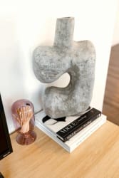 Vase en forme abstraite en béton gris, posé sur des livres empilés, à côté d'un contenant transparent avec des cure-dents, pour illustrer l'importance d'harmoniser sa décoration d'intérieur