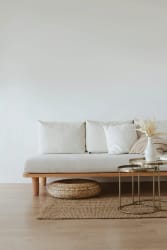 Un canapé beige avec des coussins, un plateau en verre doré, un vase avec des fleurs sèches et un pouf tissé sur un tapis, pour illustrer le service de déco rapide