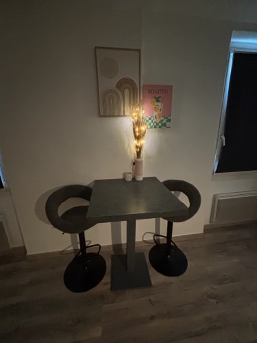 Une petite table carrée avec deux chaises hautes de chaque côté, une décoration lumineuse avec des branches lumineuses sur la table, deux tableaux accrochés au mur dont un avec le mot 'Mojito', par Inès Home Design