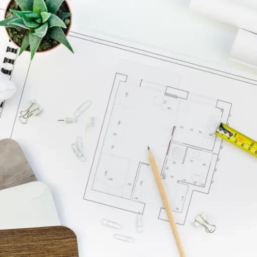 Un plan d'étage avec des outils de dessin, un crayon, des pinces à papier et une plante en pot sur une table, pour illustrer la réflexion commune sur l'espace et sa fonction