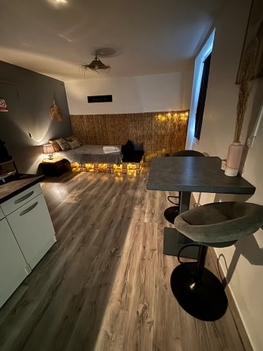 Coin salon cosy avec canapé bas sur palettes en bois éclairées, lampes tamisées, murs blanc et gris, table haute avec deux tabourets, parquet en bois clair par Inès Home Design