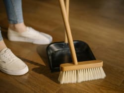 Un balai et une pelle à poussière posés sur un sol en bois, avec une chaussure sur le côté, pour illustrer le fait de nettoyer son intérieur