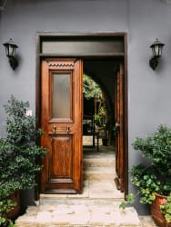 Une porte en bois ouverte donnant sur un espace intérieur, entourée de plantes vertes et de lanternes murales, sur un mur gris, pour représenter une entrée Feng Shui