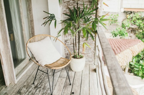 Un balcon avec une chaise en rotin, un coussin, et une plante verte dans un pot, entouré de nature.