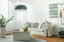 Salon moderne avec un canapé blanc, des coussins à motifs, une table basse avec des fruits et une lampe suspendue, le tout dans une pièce lumineuse avec des rideaux blancs, pour illustrer le fait d'aménager son intérieur
