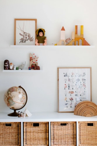 Une étagère blanche avec des objets de décoration, y compris une globe terrestre, des jouets en bois, des figurines et des illustrations encadrées, le tout dans une pièce lumineuse, pour représenter la chambre d'enfant Feng Shui