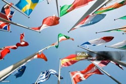 Vue en contre-plongée de plusieurs drapeaux de pays flottant sous un ciel bleu clair.