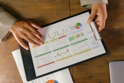 Une personne tenant un document de présentation avec des graphiques et des tableaux colorés sur un bureau en bois, pour illustrer l'accompagnement sur les marchés par Pro Mundi Conseil
