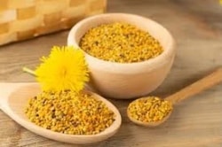 Deux bols en bois remplis de pollen de fleurs dorées, avec une fleur jaune à côté, sur une surface en bois.