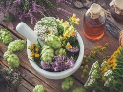 Mortier en céramique rempli de plantes aromatiques et médicinales, avec un flacon d'huile à côté, sur une table en bois.