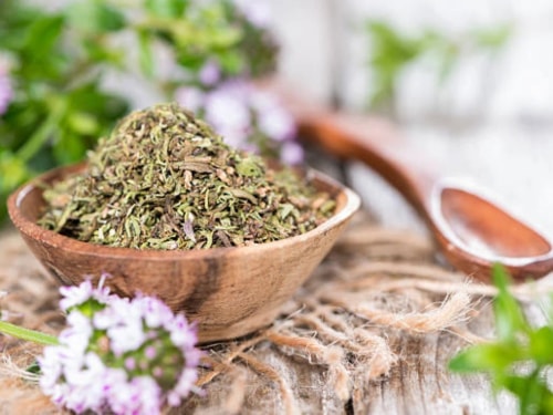 Un bol en bois rempli d'herbes sèches avec des fleurs violettes floues en arrière-plan.