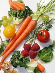 Un assortiment vibrant de légumes frais comprenant des carottes oranges, des feuilles de chou, des tomates rouges, des raisins verts, des framboises et des noix, disposés artistiquement sur une assiette blanche.