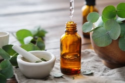 Bouteille en verre ambré avec un compte-gouttes, entourée de feuilles vertes, un mortier avec des herbes à côté, sur une surface en bois