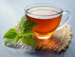 Tasse de thé fumé posée sur un dessous de verre en jute avec des feuilles fraîches à côté.