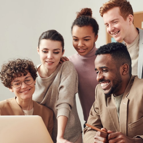Cinq personnes regardent un ordinateur portable avec intérêt, souriant et interagissant ensemble dans un environnement accueillant.