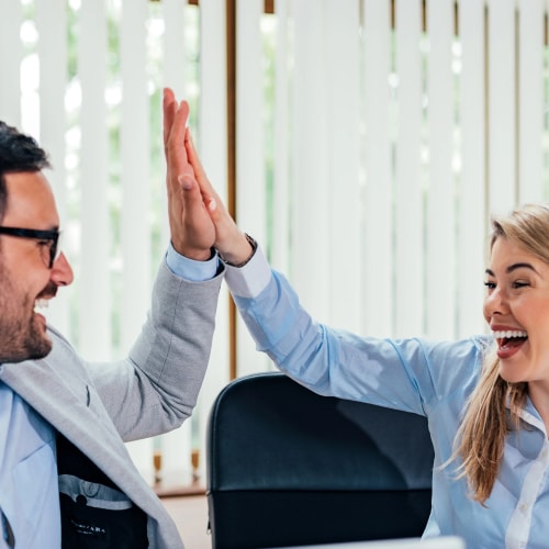 Deux personnes au bureau se donnant une tape dans la main avec le sourire.