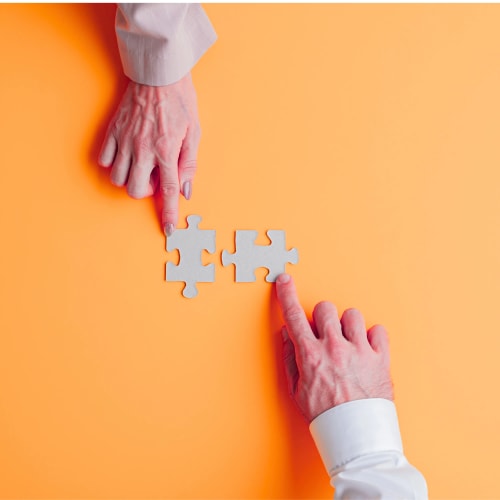 Deux mains atteignant des pièces de puzzle sur un fond orange.