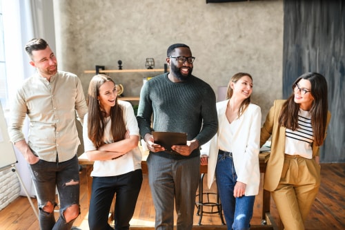 Un groupe de cinq personnes souriantes se tenant ensemble dans un bureau moderne, avec un homme tenant une tablette au centre.