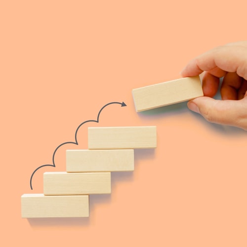Une main tenant un bloc en bois tandis que d'autres blocs sont empilés sur fond orange.