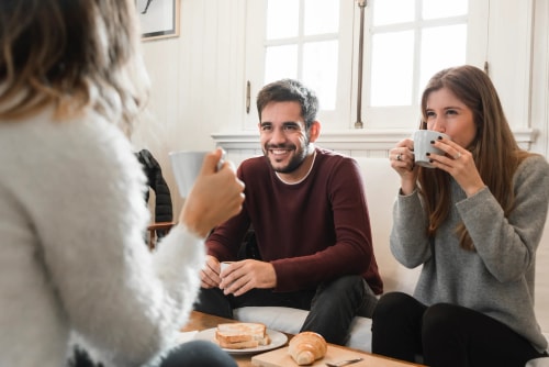 Trois jeunes amis sont assis autour d'une table, buvant du café et discutant joyeusement lors d'un petit-déjeuner convivial.