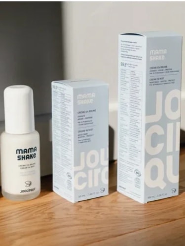 Ventre de femme enceinte avec une trace de crème hydratante, tenant un tube de lait corporel Daylily Paris sur un lit.