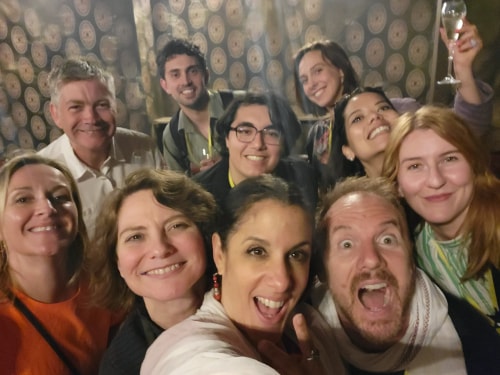 Groupe de neuf personnes souriantes prenant un selfie lors d'une soirée, une femme tenant un verre de champagne levé en arrière-plan.