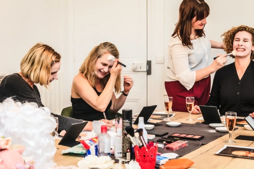 Groupe de femmes assises autour d'une table, appliquant du maquillage et riant ensemble dans une ambiance conviviale.