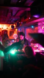 Personne habillée de façon extravagante dans un bar ou une boîte de nuit avec des lumières colorées et ambiance festive.