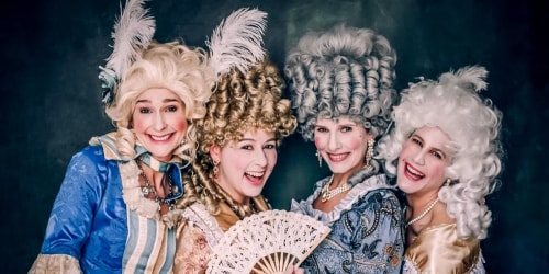 Une femme avec des boucles, portant une robe blanche et des bijoux, est appuyée contre une porte en bois foncé avec un panneau indiquant "Bienvenue au cabinet des curiosités".