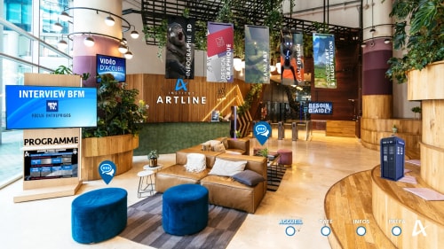 Intérieur moderne et accueillant d'un institut artistique avec un canapé en cuir marron, des poufs bleus, des plantes vertes, plusieurs panneaux suspendus indiquant des domaines comme infographie 3D, design graphique, game art, game design, concept art et illustration, un écran affichant une interview BFM et un espace d'information avec un programme, le tout dans un espace lumineux avec du bois et du verre.