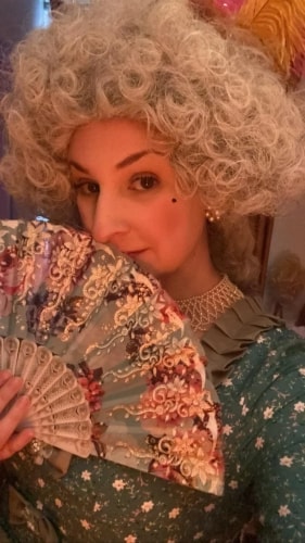 Personne posant dans une robe noire et portant de grands boucles d'oreilles brillantes, encadrée par un cercle lumineux rouge orangé.