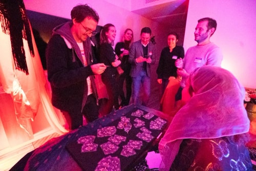 Groupe de personnes réunies autour d'une table avec des cartes, dans une ambiance lumineuse rouge, certaines souriantes et regardant des objets dans leurs mains.
