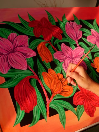 Une main tient un pinceau pour peindre des fleurs colorées et des feuilles vertes sur un fond noir, le tout encadré par des bordures orange vif.