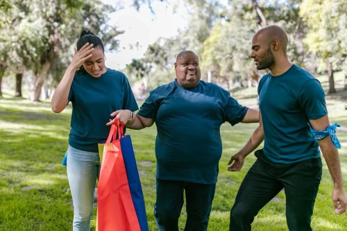 Trois personnes portant des t-shirts bleu marine marchent dans un parc. L'une d'elles tient un sac aux couleurs vives tandis qu'ils discutent joyeusement.