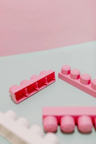 Des briques de construction en plastique rose posées sur une surface vert pâle, avec un fond rose pastel.