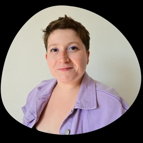 Portrait de Margaux Alloucherie, agitatrice de savoirs expérientiels, portant une veste en jean lilas et souriant devant un fond blanc.