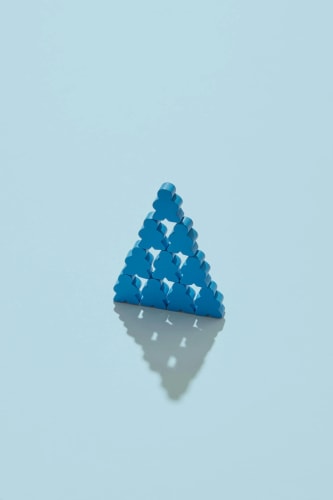 Une pyramide composée de dix petits personnages en bois bleu sur un fond bleu clair avec une ombre portée.