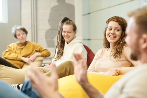 Un groupe de jeunes adultes assis sur des poufs discutent joyeusement dans un espace de bureau décontracté.