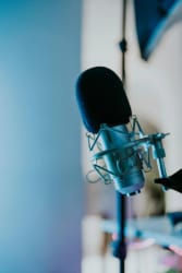 Un microphone de studio professionnel avec une bonnette anti-vent noire, monté sur une suspension élastique dans un environnement aux tons bleutés.