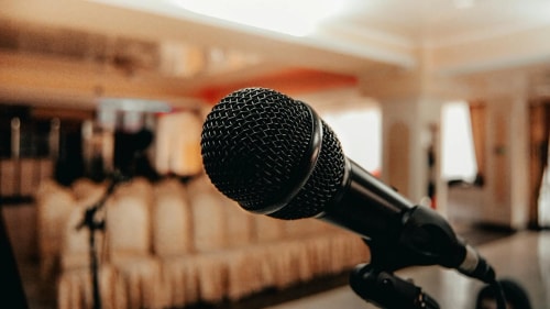 Un microphone noir est positionné en premier plan, avec une salle de conférence floue en arrière-plan.