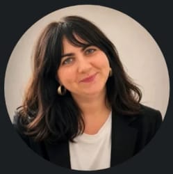 Portrait d'une femme souriante aux cheveux bruns, portant un t-shirt blanc et une veste noire, photographiée dans un cadre circulaire.