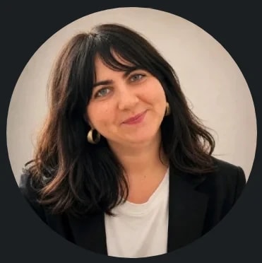 Portrait d'une femme souriante aux cheveux bruns, portant un t-shirt blanc et une veste noire, photographiée dans un cadre circulaire.