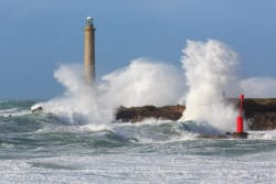 Un phare se dresse sur une côte rocailleuse, avec de fortes vagues déferlant contre les rochers et un phare rouge sur le bord.
