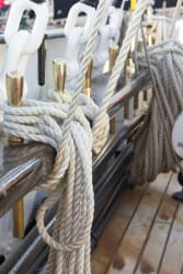Gros plan sur des cordages et des attaches en métal sur un bateau, avec un fond en bois.