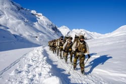 Groupe de soldats marchant en formation en montagne, entourés de paysages alpine et de sommets enneigés.